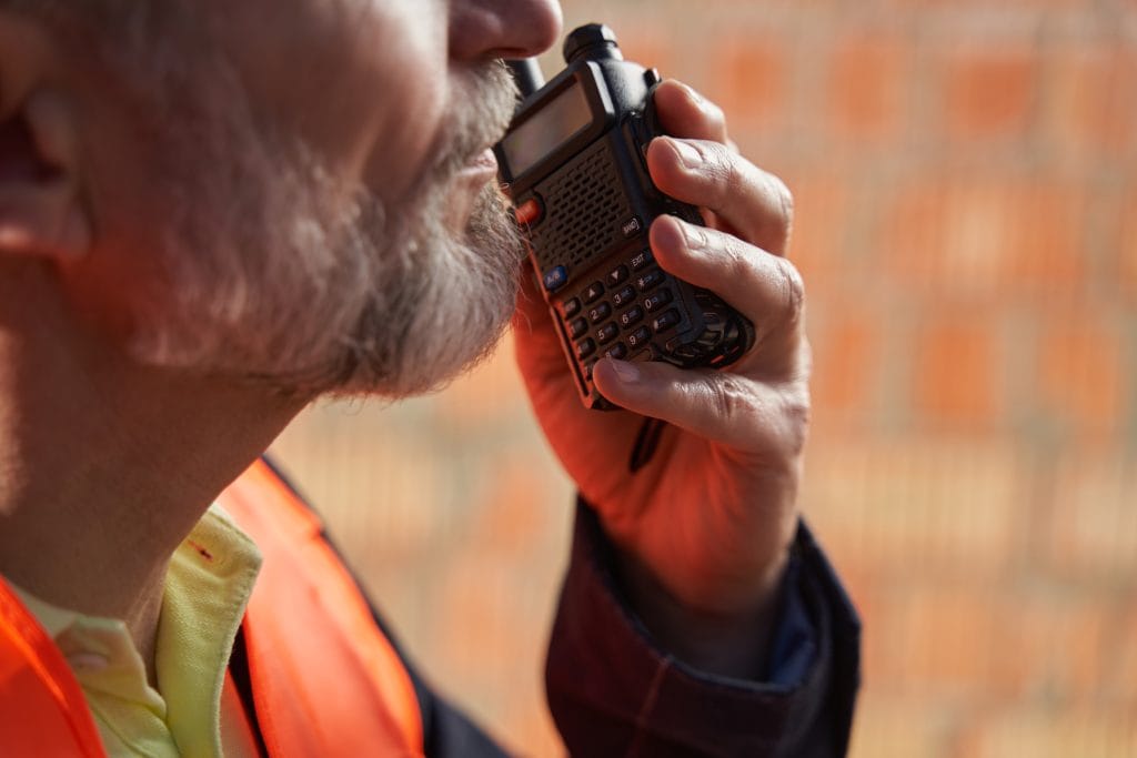 Cropped photo of a bearded builder holding a walkie talkie close to his mouth
