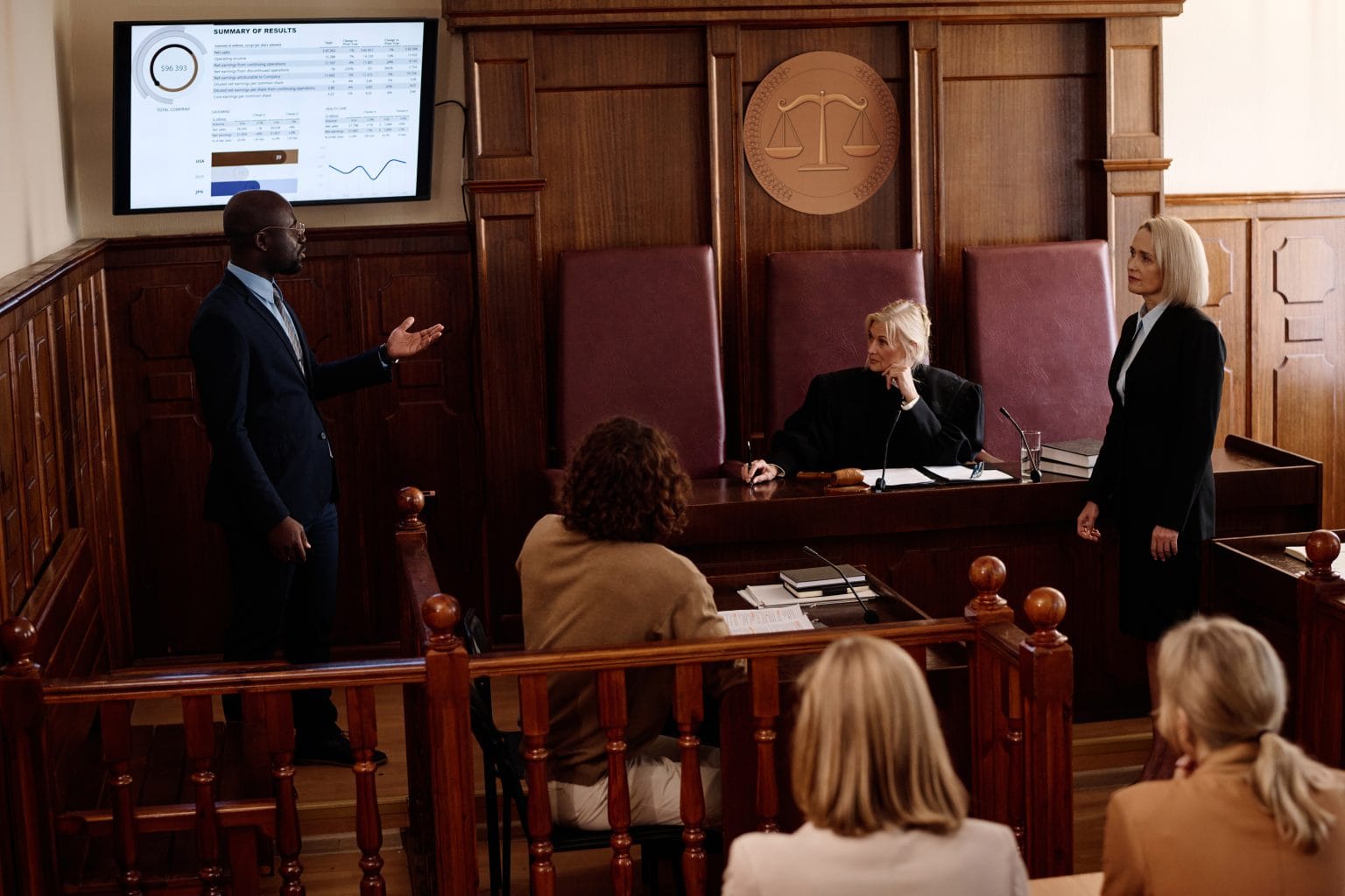 Young confident African American attorney making presentation of summary of results while standing by screen with statistic data