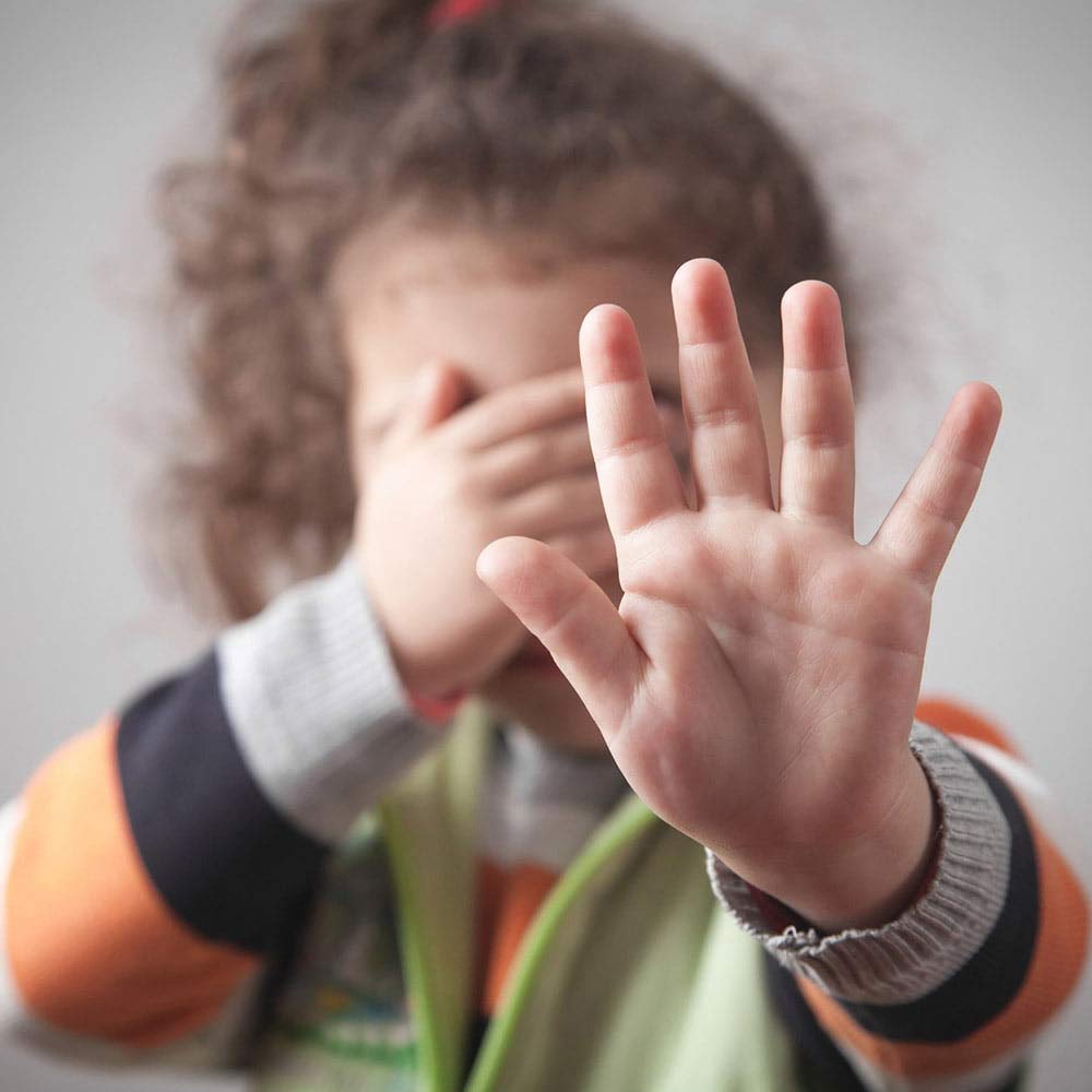 Child Abuse - A child holding out their hand while covering their face.