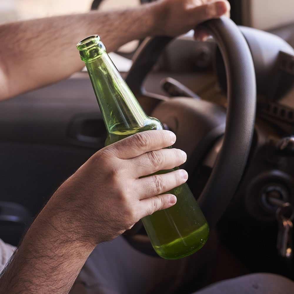 Drunk Driving - A man holding a beer bottle while driving a motor vehicle.